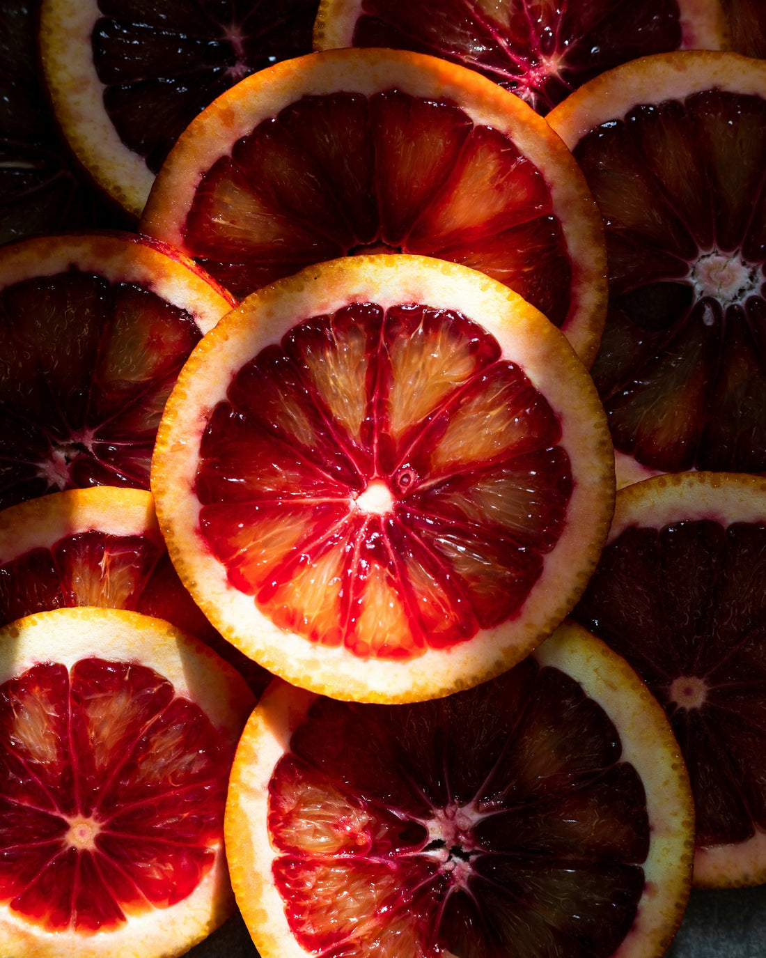 Halved blood oranges with deep ruby-red centers on a neutral background